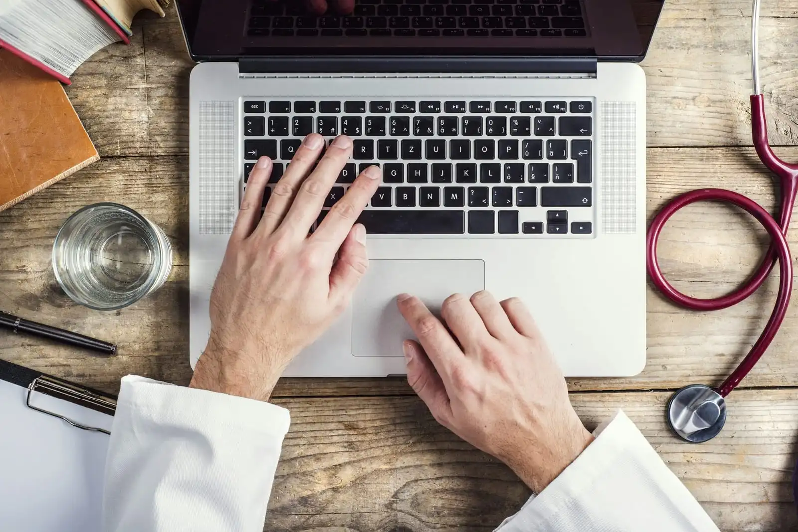 Doctor writing at a laptop, hands and desk in focus